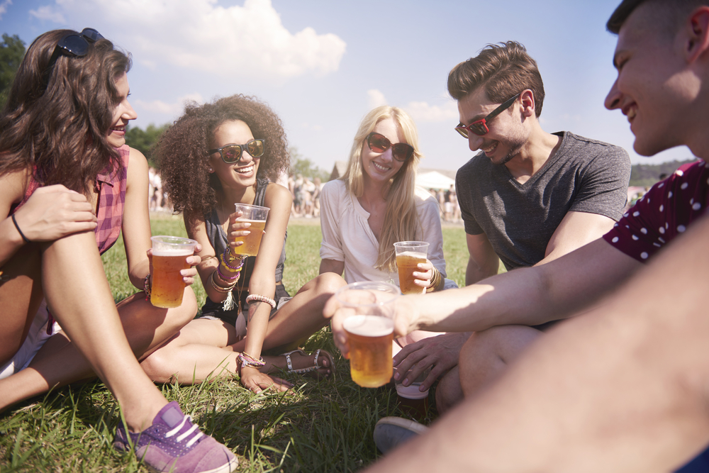 Five friends laughing on the lawn at North Carolina Brewers and Music Festival listening to music and enjoying a beer. 