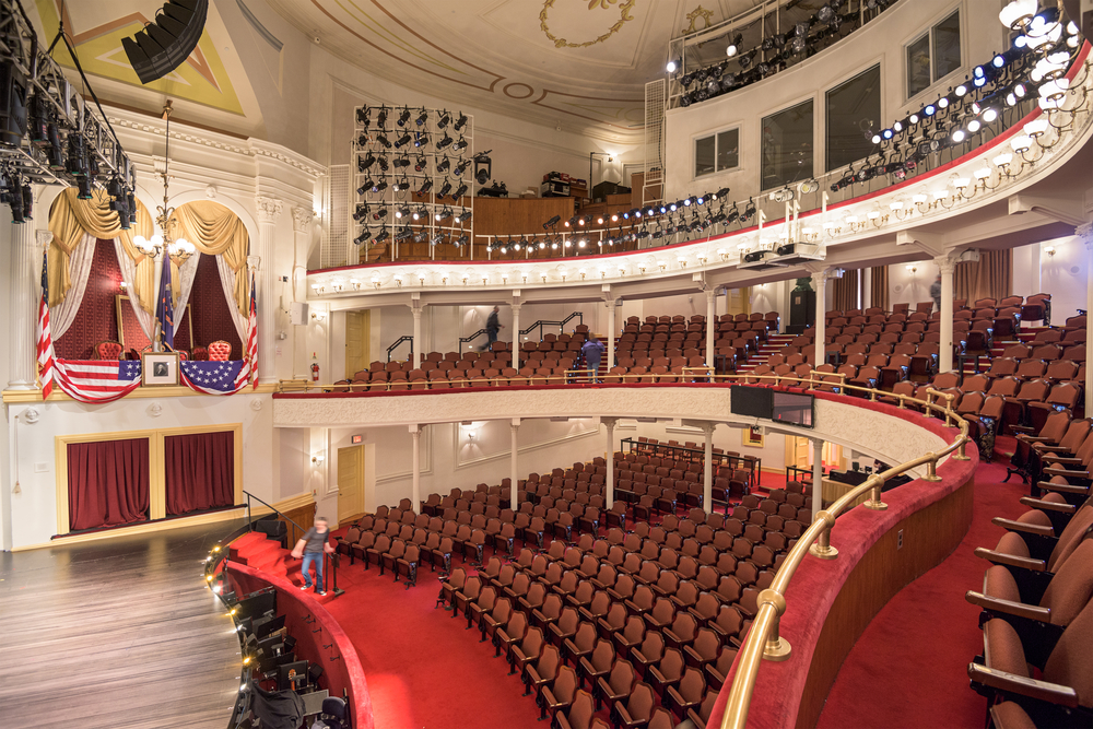 inside of the fords theatre with the stage on the left and the seating on the right, two balcony seats are just above the stage 