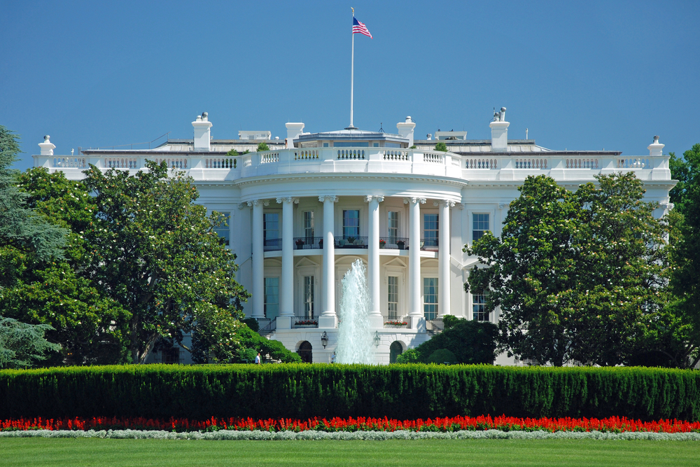 photo of the white house  on a bright clear day with an american flag flying on top