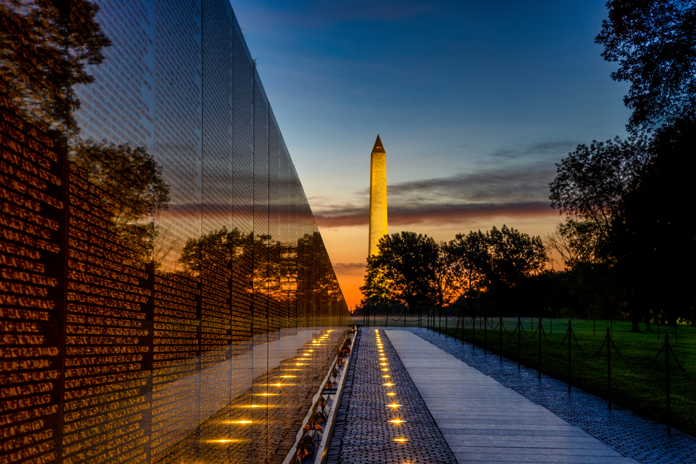 long wall of veterans names on the left with the Washington monument in the background at sunset 