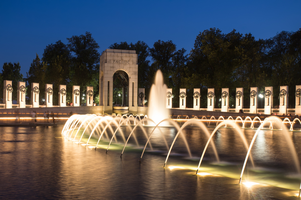 fountains are arching in the water in front of the world war 2 memorial at night, there are lights under the fountains, one of the best landmarks in Washington DC 