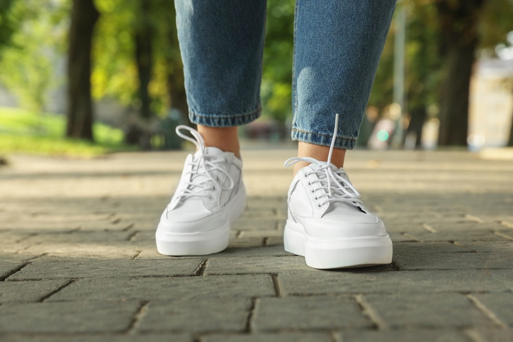 Close-up of stylish, white sneakers walking down a sidewalk.