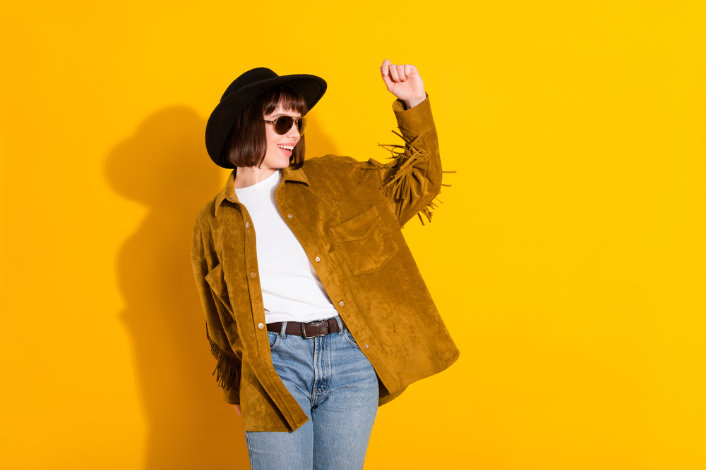 women against yellow background with fringe jacket on and sun glasses. The article is about what to wear in Nashville