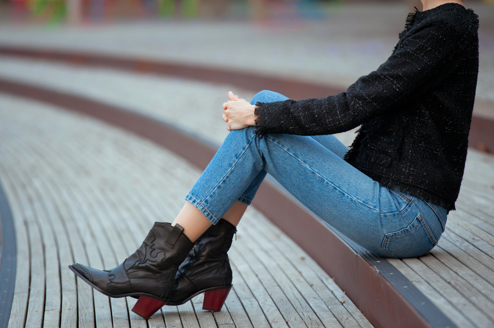 women with boots, jean and a jacket sat down. 