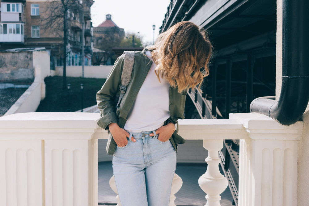 a girl looking down in jeans, white tee shirt and green army jacket