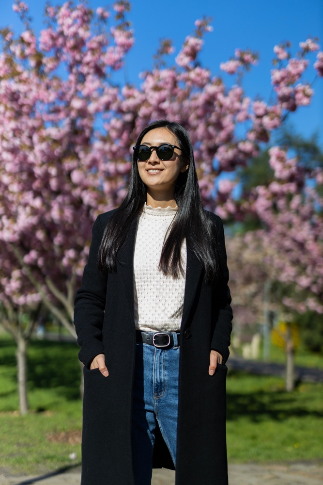 a girl in jeans , black coat and white shirt standing in front of cherry blossoms