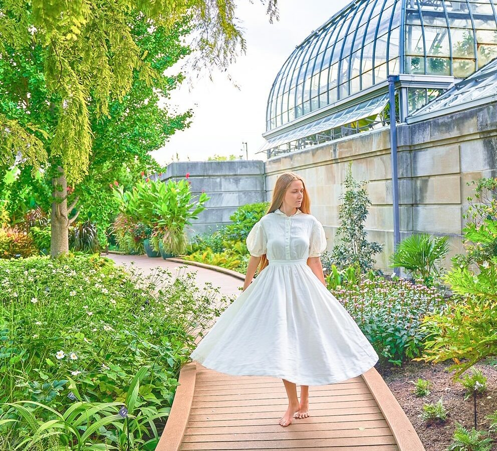 a girl in white dress walking in botanical garden