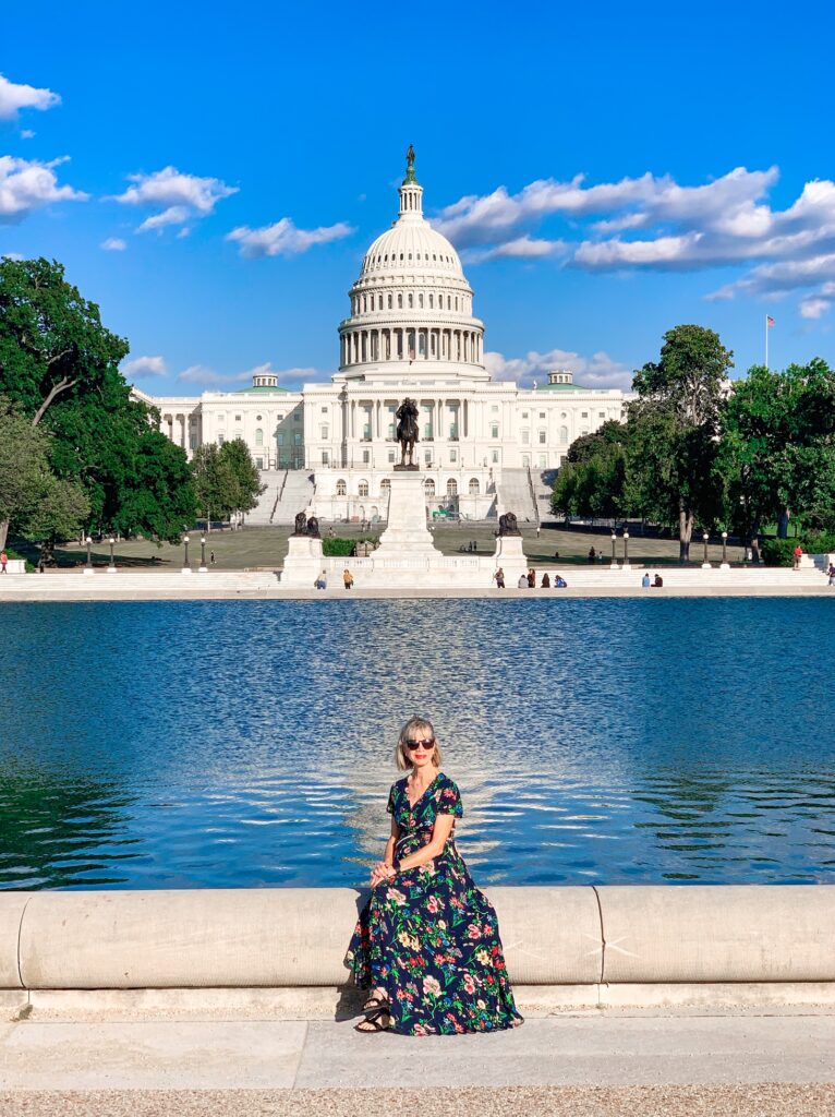 a girl in a dress sitting on the reflection pond in front of the US Capitol building. 