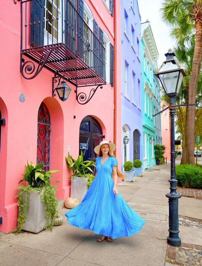 woman standing in a blue dress in Charleston in front of cute colored buildings