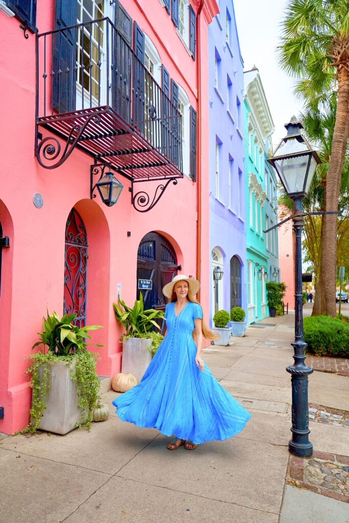 a woman is twirling in a blue dress on the sidewalk in front of a row of colorful houses in one of the best charleston sc outfit ideas 