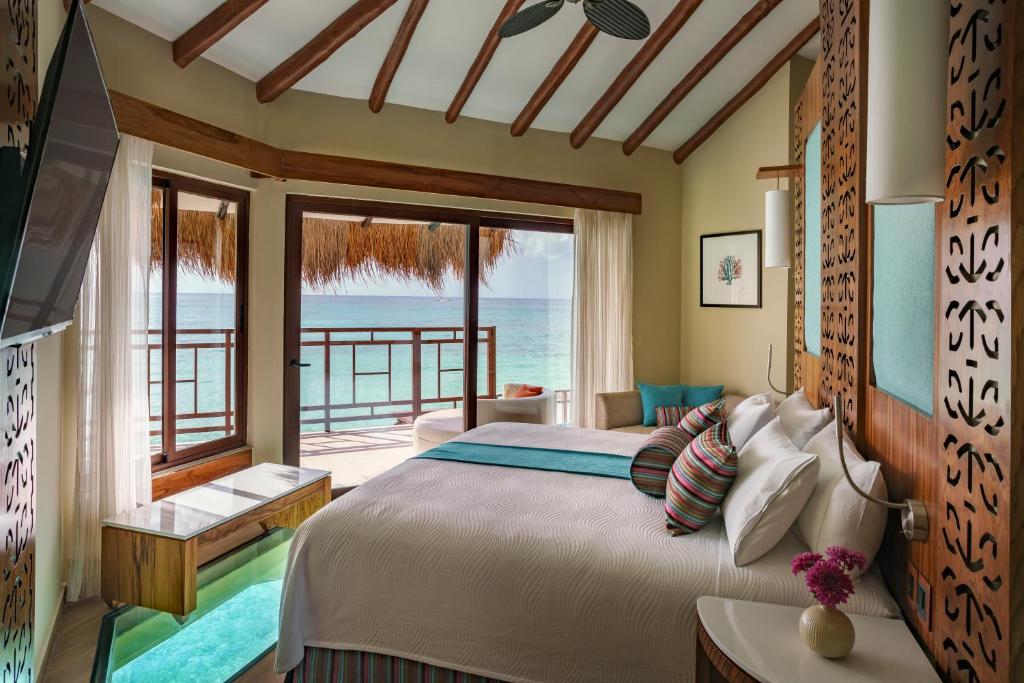 inside of a water bungalow showing a bed and huge glass windows overlooking the water.  One of the best Overwater Bungalows Near The South.