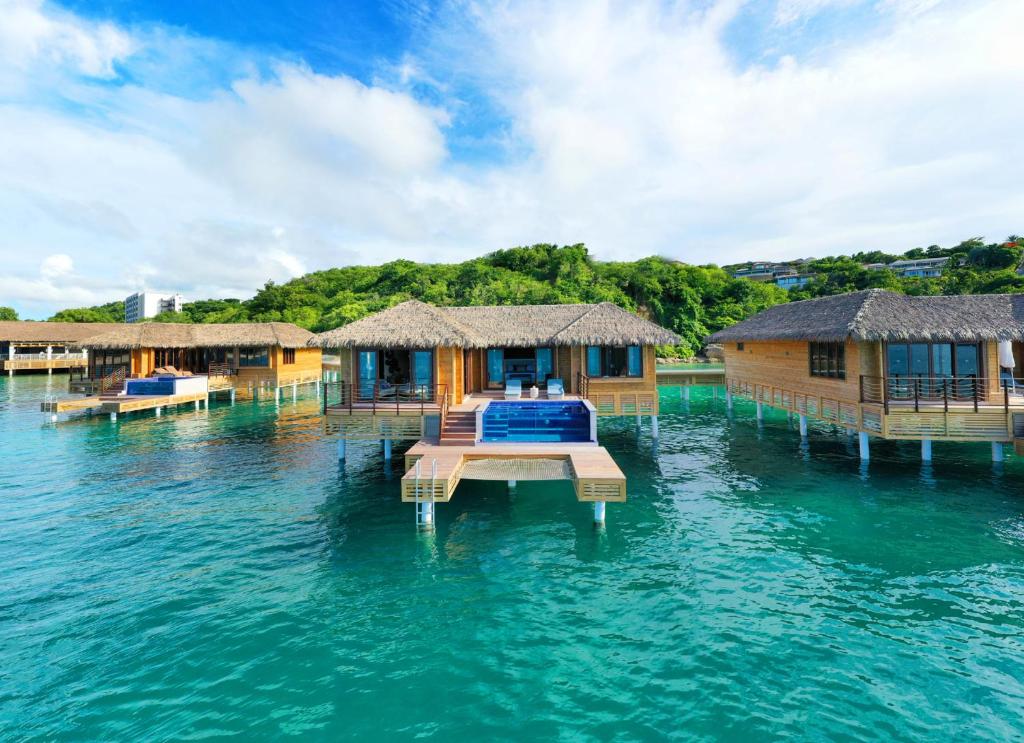 overwater bungalow with thatched roof and pool standing in blue water with blue sky and clouds. the building is brown