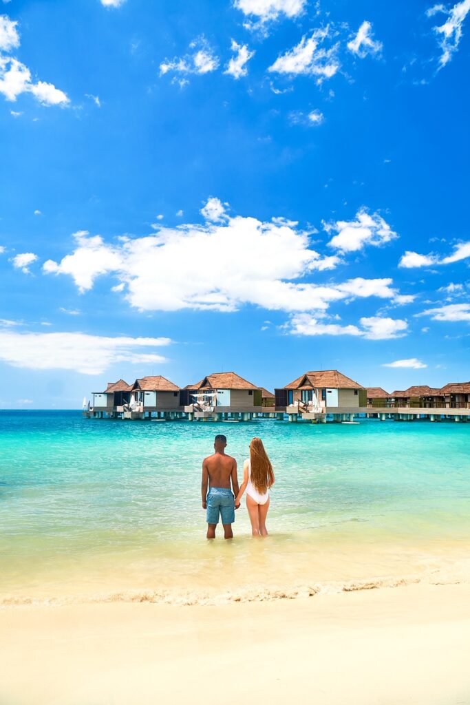 A couple standing on the beach looking towards some water bungalows over the sea. Article is about Overwater Bungalows Near The South.