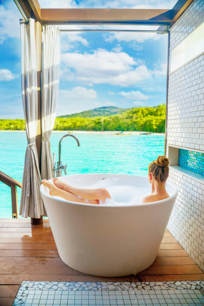 Girl in a bath on the balcony overlooking the water with greenery in the background.