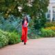 A woman in red pants, matching top, and red sunglasses skips down the sidewalk at a botanical garden, knowing what to wear in Atlanta.