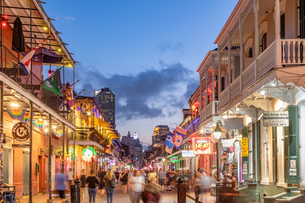 A shot of Bourbon street at night shows guests walking down the street, nestled between buildings, all aglow in dusk.