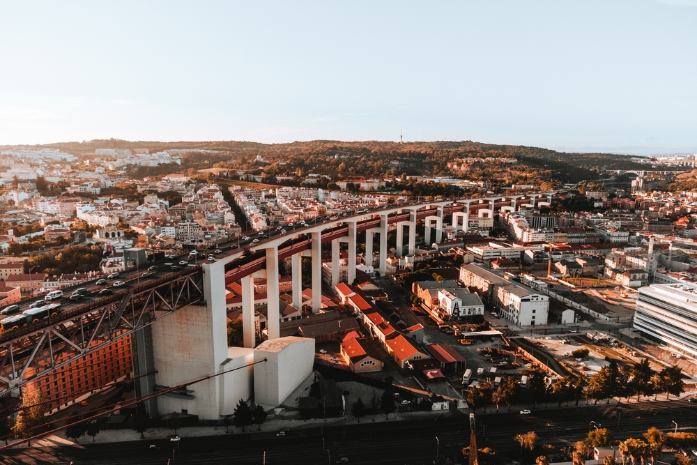 An overhead shot of Lisbon, which is one of the international options for the cheapest places to fly from Dallas, shows colorful buildings and bridges in a vibrant city. 