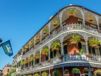 A photo of some of the most historic and stunning buildings in NOLA shows a three story building with lush hanging plants over each window and balcony.