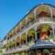 A photo of some of the most historic and stunning buildings in NOLA shows a three story building with lush hanging plants over each window and balcony.