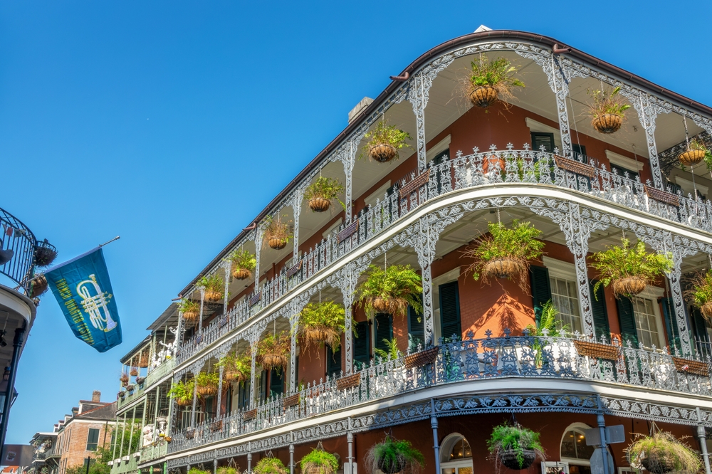 A photo of some of the most historic and stunning buildings in NOLA shows a three story building with lush hanging plants over each window and balcony. 