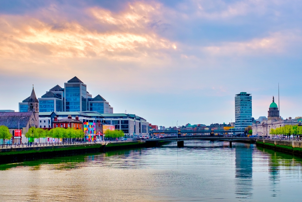 In a dusk filled sky, the light setting, Dublin's city, which is one of the cheapest places to fly from Washington D.C., is vibrant against the river that cuts through the city, its buildings colorful and tall and green! 