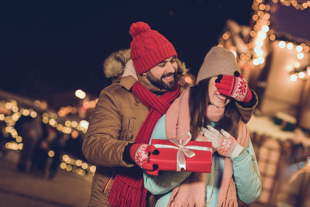 girlfriend boyfriend getting gift package walking outdoors Christmas market. The article is about Christmas in the South USA. 