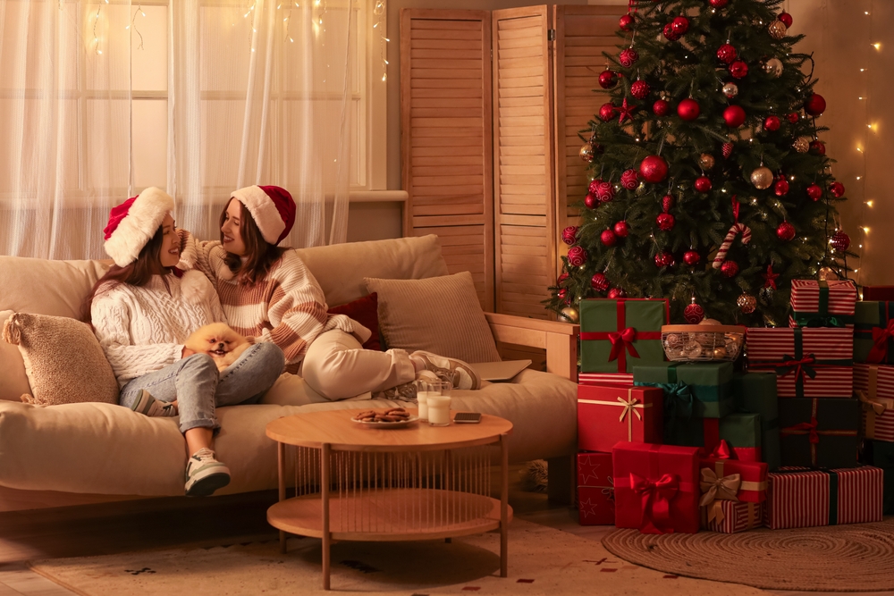 Young lesbian couple in Santa hats with dog sitting at home on Christmas eve