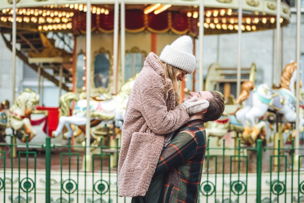 Boyfriend and girlfriend having fun on a Christmas market wearing warm clothes. Outdoors, winter time, snowy weather. Article is about Christmas Towns in the South.