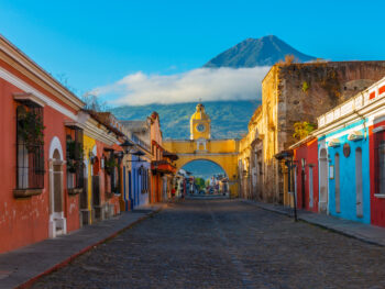 Cityscape of the main street and yellow Santa Catalina arch in the historic city center of Antigua at sunrise with the Agua volcano, Guatemala.